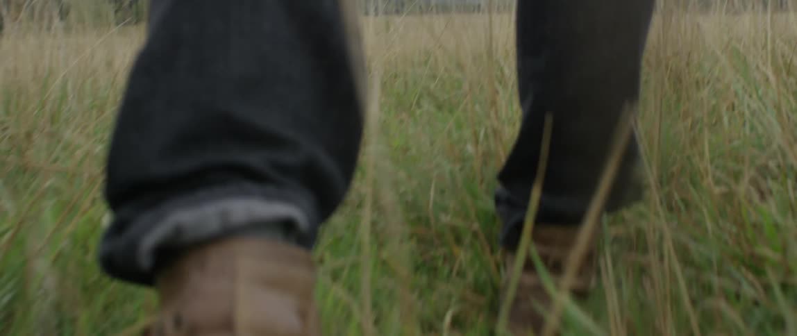 View of persons lower legs and boots as they walk through a field