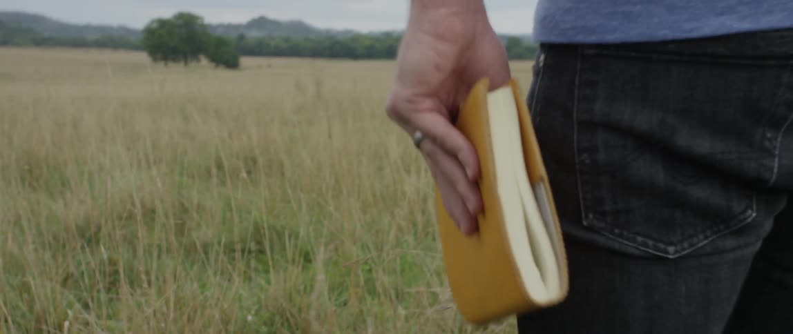 Man holding a notebook walks through a field