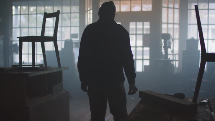 A carpenter checks the chairs inside a dimly lit workshop