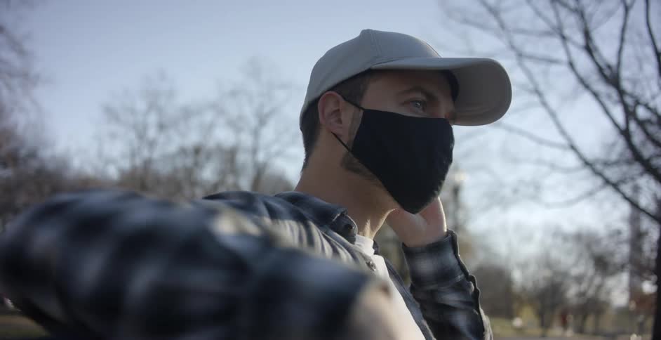 A man sitting outside puts a mask on