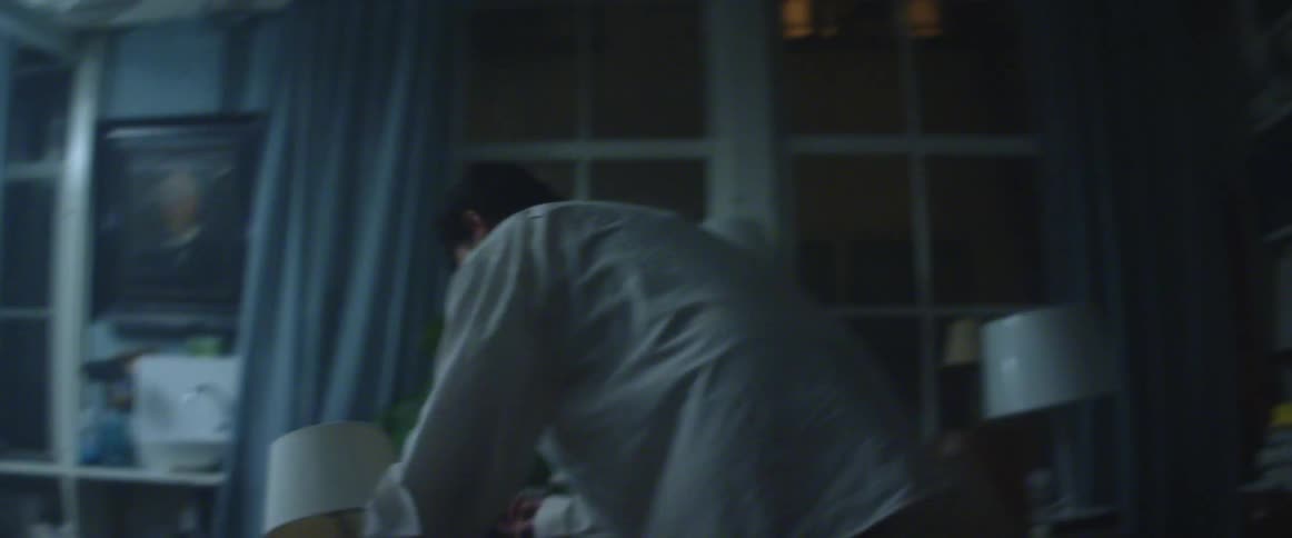 A person picks up lamps fallen on the floor of a dimly lit living room at night