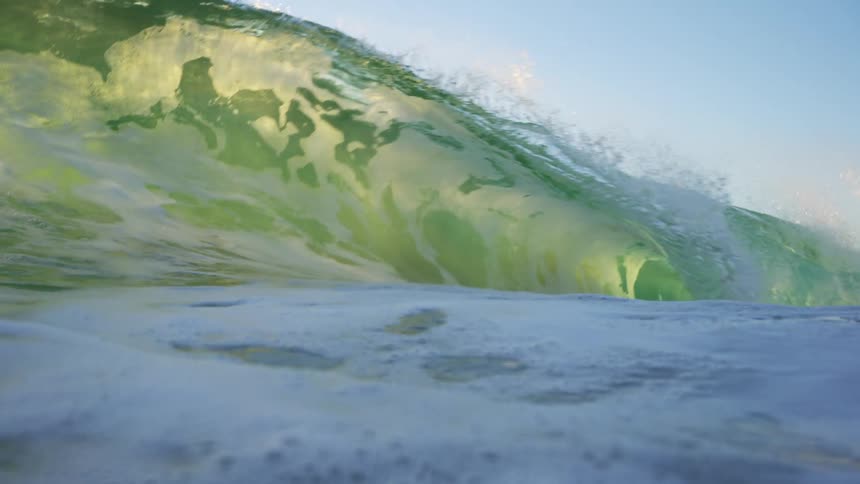 Green water wave crashes under clear blue sky
