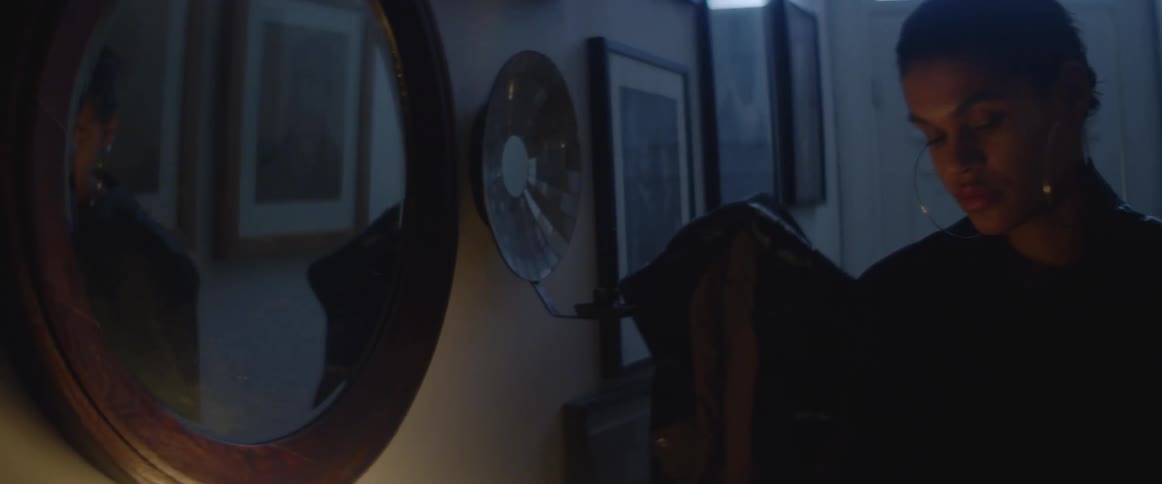 Young woman standing on a dimly lit narrow corridor at home reflecting on a mirror