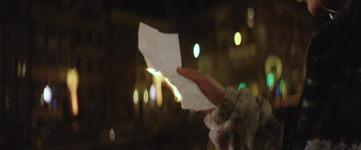 Woman wearing a fur coat uses a lighter to burn a piece of paper at night