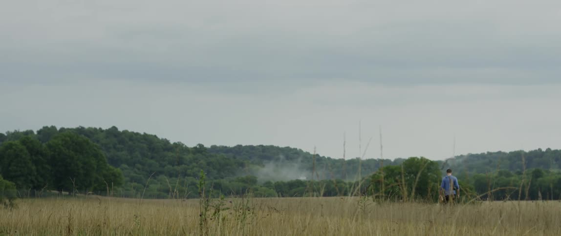 A man is hiking along a grass covered field