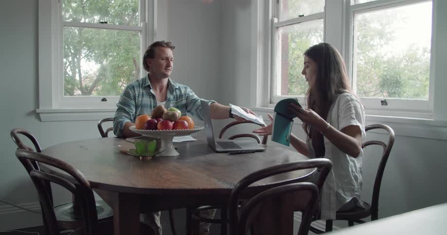 A man and woman sit at a dining table trading reading material