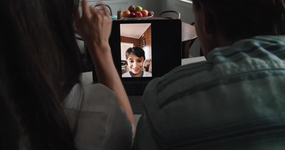 Mom and dad talk to their son on a laptop while sitting in a kitchen at a counter