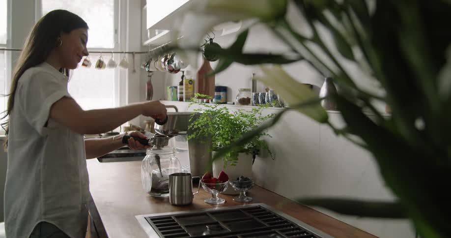 A woman prepares coffee standing at the counter in a kitchen