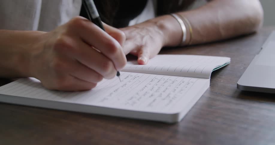 A teenager writes in a notebook as she sits a desk