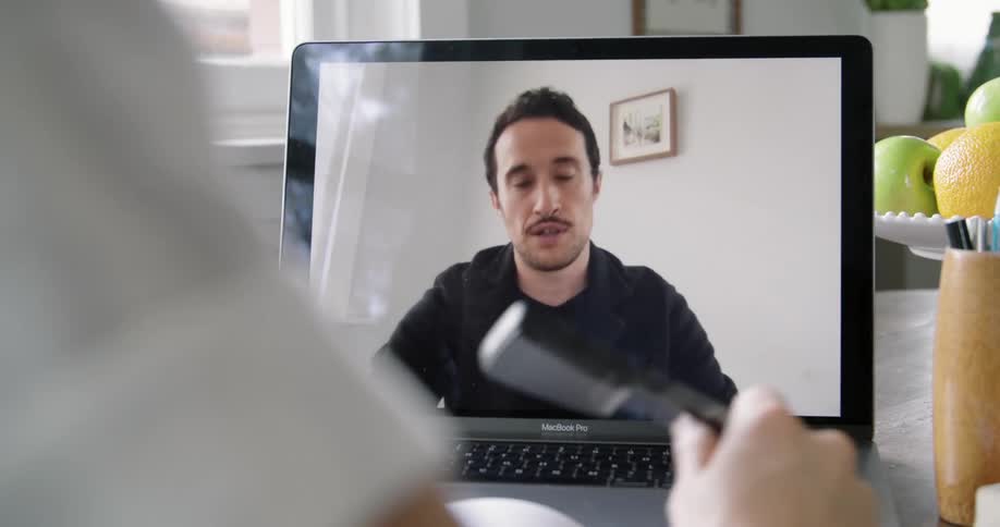 A woman writes in a notebook while talking with a man over video chat