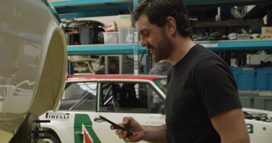 Mechanic sending a text on a smartphone while fixing a car in a shop