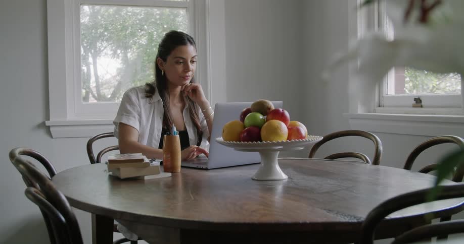 Young woman working from home types on a laptop on the dining table