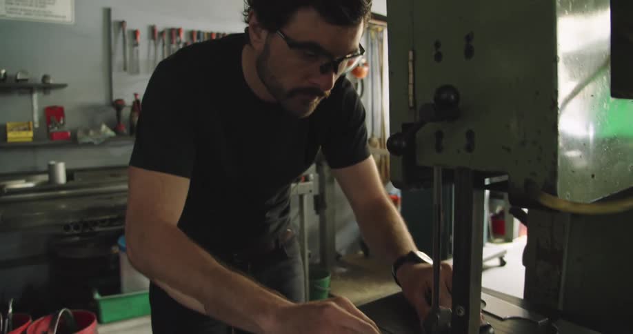 A man in a workshop uses a machine to cut metal