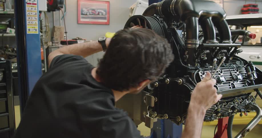 A mechanic assesses an engine in a garage holding a wrench