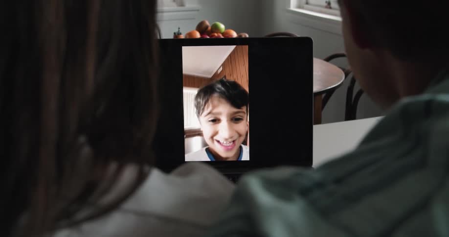 A man and woman at home video chat on a laptop with their son
