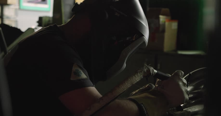 A man in a shop puts the visor down on his helmet and starts to weld