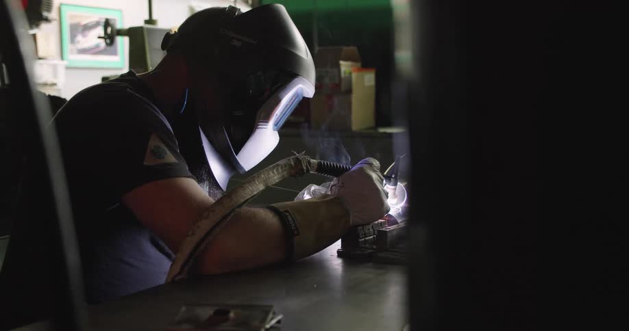 A person welds an object while sitting at a counter