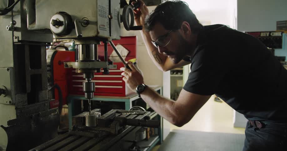 A man drilling holes in metal in a workshop