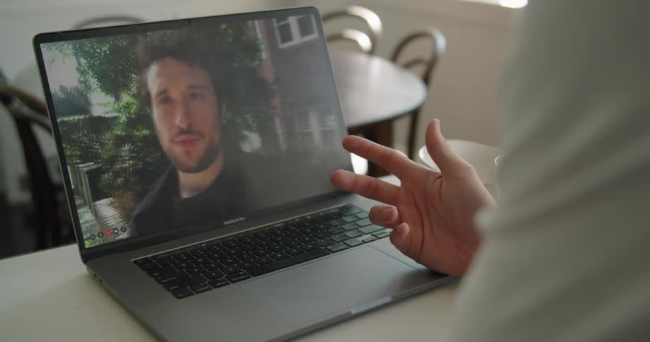 Man on a laptop monitor talks with someone that is sitting at a desk while looking at the laptop screen