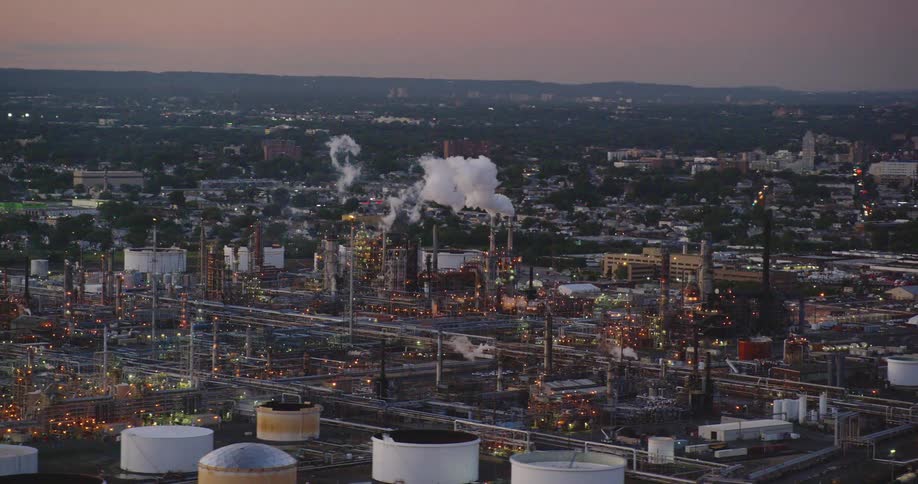 Smoke billows into the the air from a large factory in a city at sunset