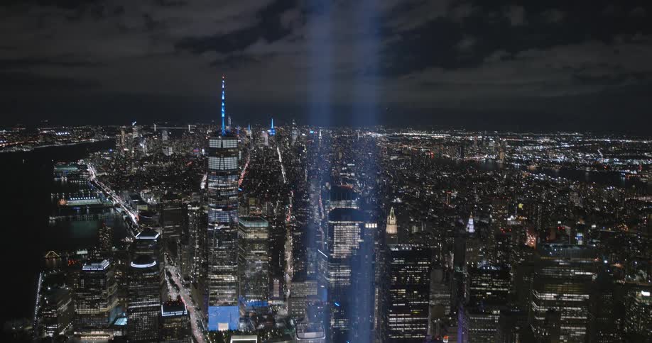 Nighttime view of the 911 memorial light into the sky with surrounding city buildings