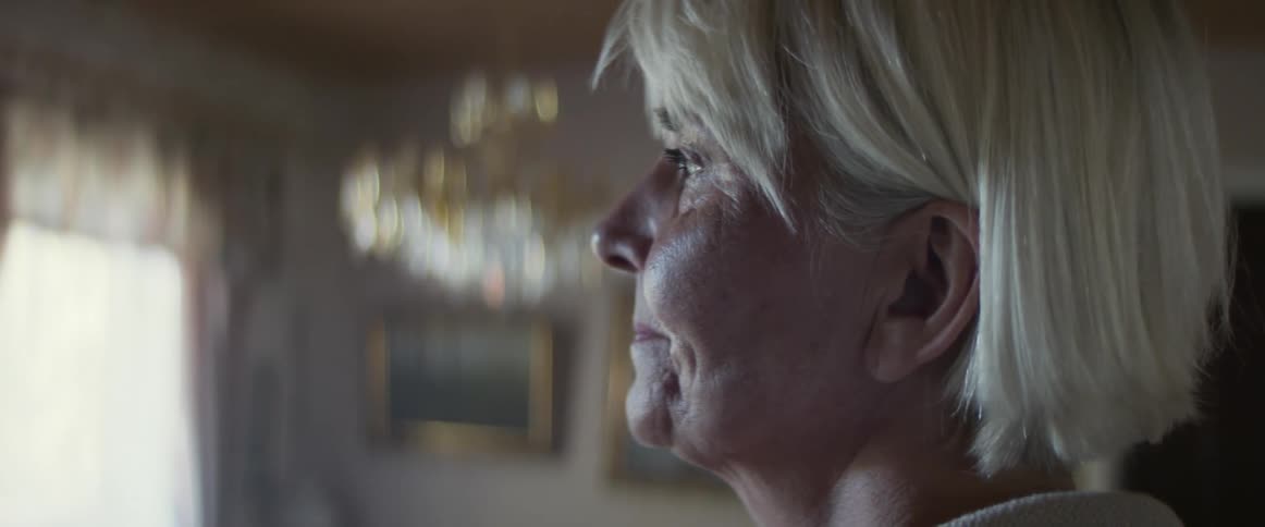 An elderly woman standing in a house looking sad
