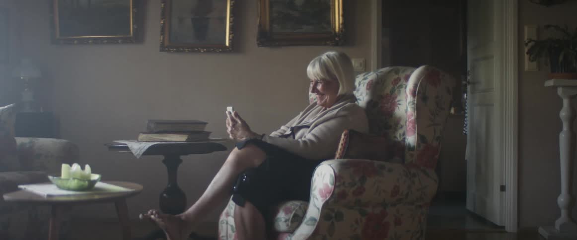 Blonde middle aged woman sitting in an armchair makes a video call on a smartphone