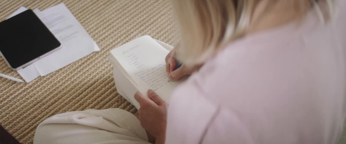 Woman with a white pants and a pink sweater writes things down in a notebook