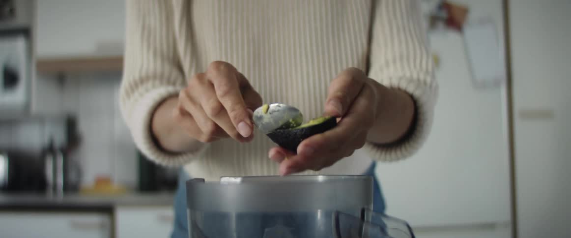 A woman scoops the inside of an avocado into a pitcher