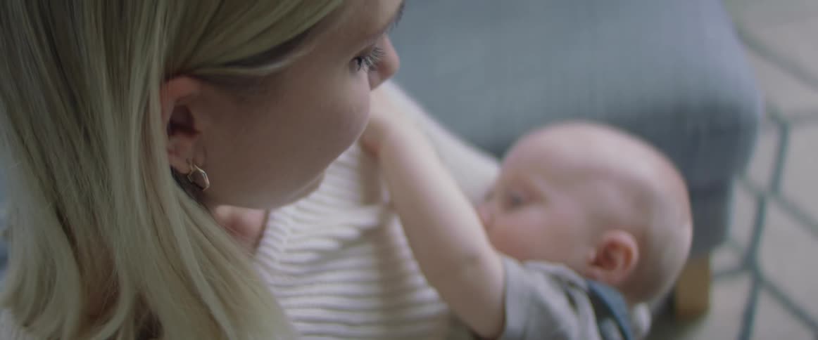 Mother with a white knit sweater breastfeeds her baby in living room