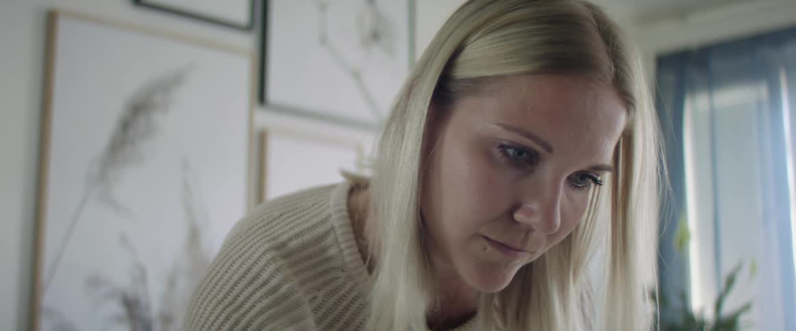 A blonde woman leans over to look at something in her living room