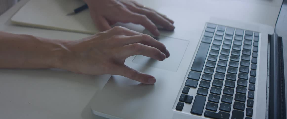 Woman working at home writes in a notepad with a pen and then uses a laptop