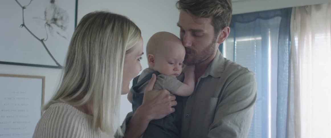 Father with a beard and a shirt holds his baby and talks to blonde mother