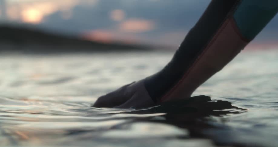 Hand touching the surface of the ocean waters near the coast at sunset