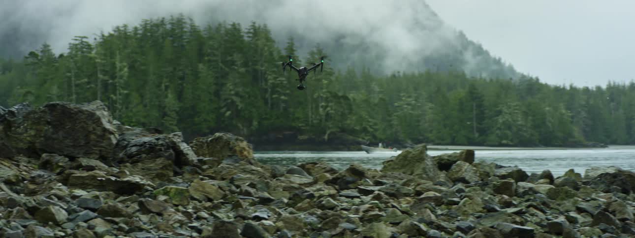 A drone flying over rocks across the lake in the wilderness