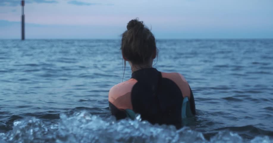 A woman standing in the ocean in a wet suit looks around