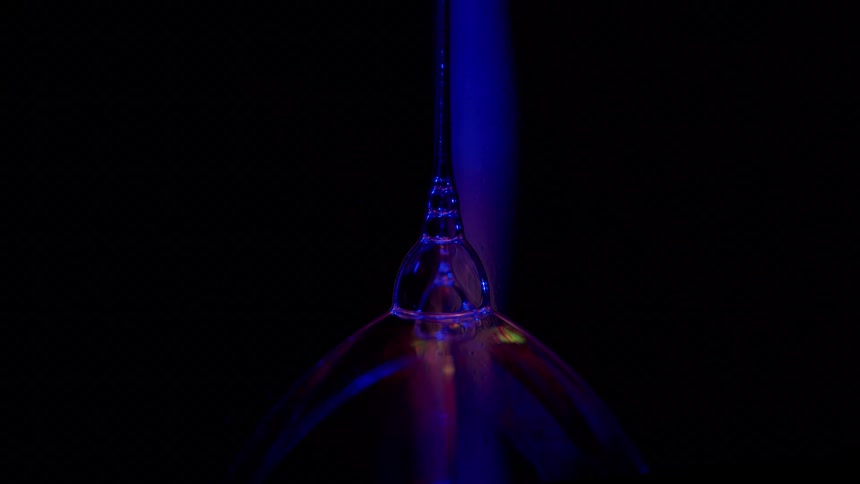 Fluorescent fosforescent clear liquid pouring over a glass dome shining blue under ultra violet light