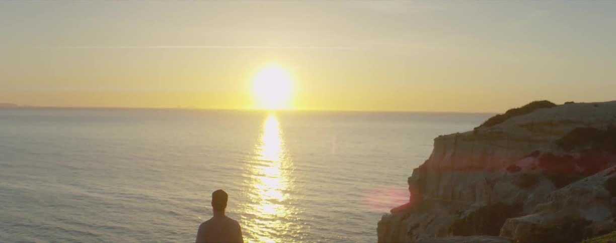 Man stands near ocean and watches sunset in an orange sky