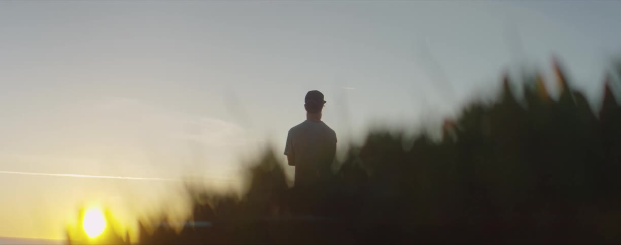 A man stands outside on grass looking at a low sun in the sky