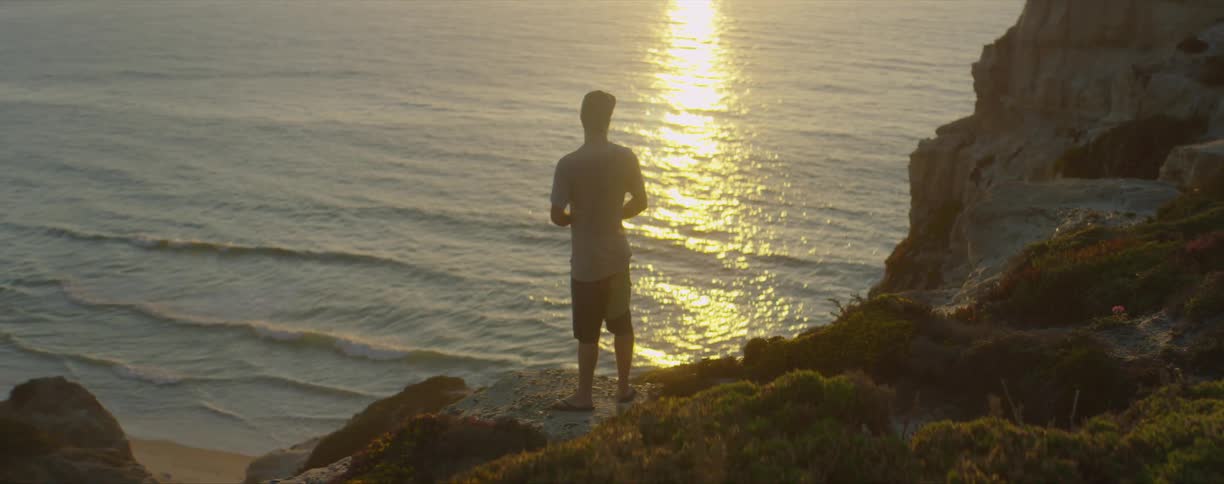 A man standing on top of a rock enjoying the sunset at the beach