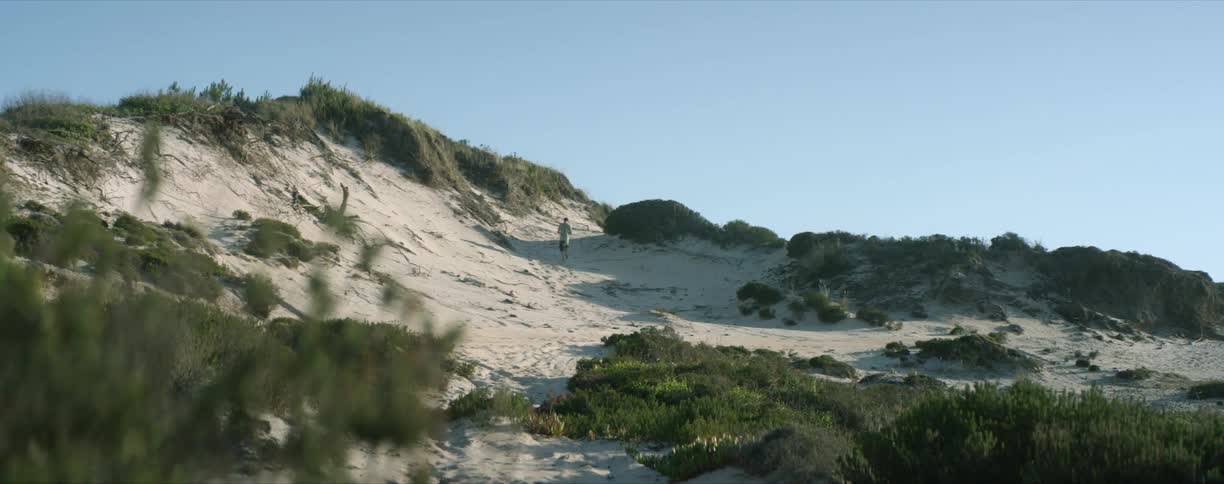 A man walks down the side of a shallow hill on the beach