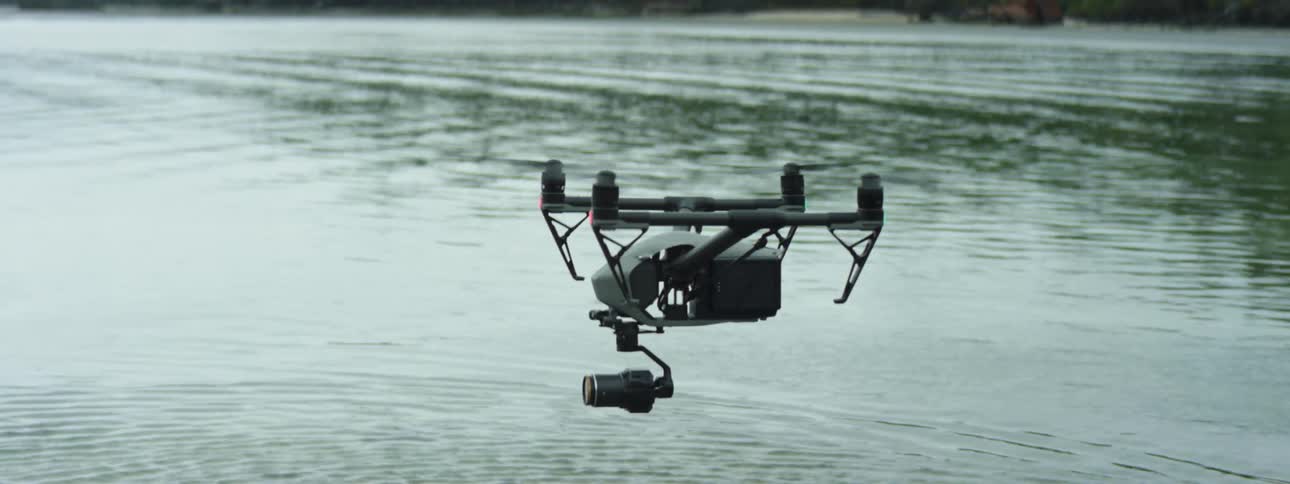 A person with a controller flying a drone with a camera over a lake
