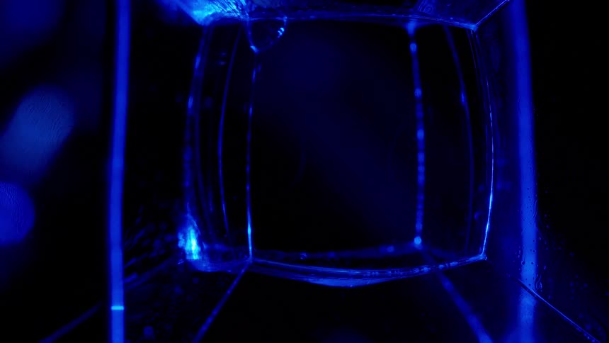 Fluorescent fosforescent liquid dripping inside a square container shining blue under ultraviolet lights
