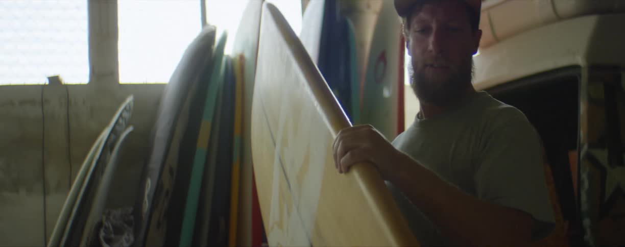 Man picks up and inspects a surfboard before setting it down to work on it