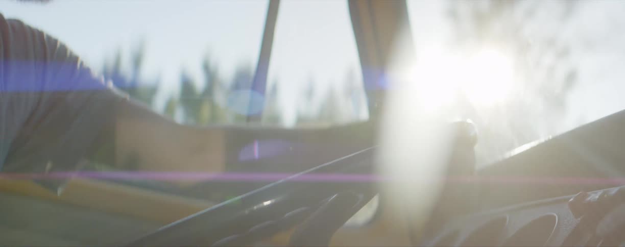 Bearded man driving a truck with one arm on the steering wheel on a sunny day