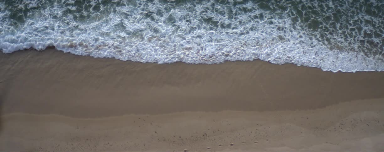 Ocean waves slowly roll into a sandy beach during the day