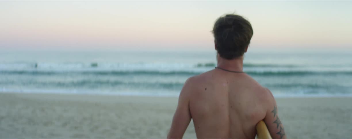 A man holds a surfboard as he walks towards the ocean