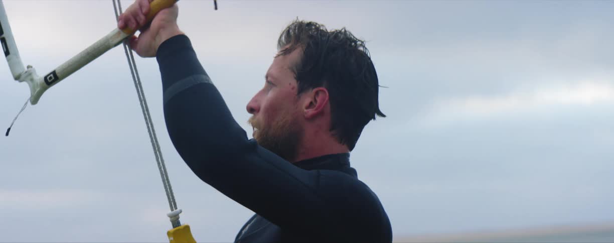 Bearded man holding the handle of a kite surf in the ocean at day