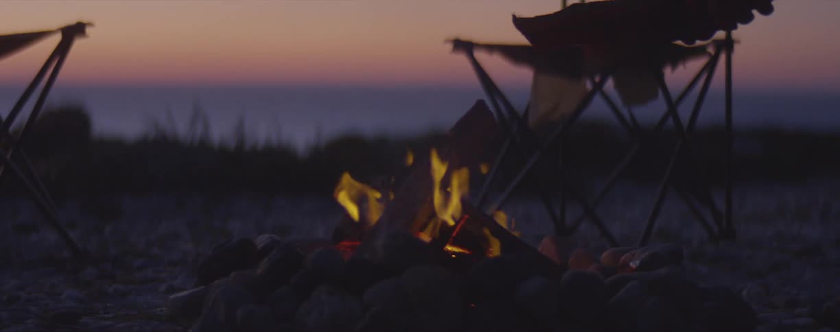 A person places wood in a campfire at sunset