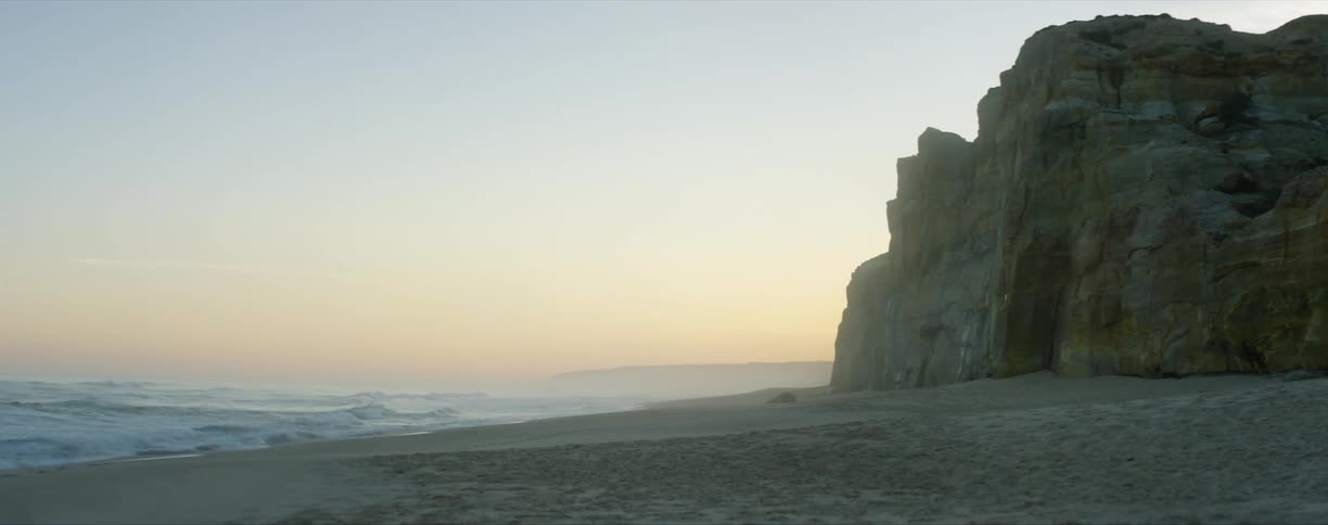 A beach with a cliff and calming waves at dusk